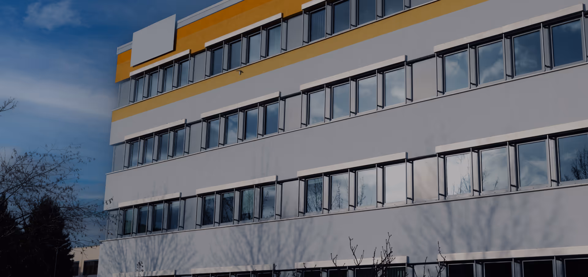Mehrstöckiges Bürogebäude mit weißen und gelben Fassaden und vielen Fenstern unter blauem Himmel.